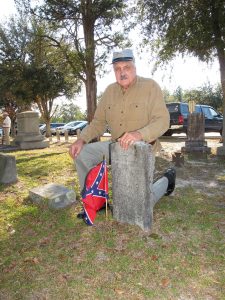 Dressed as a Confederate Soldier, Fritz Jolly kneels beside the grave of Drummer Boy William Woodward Macon who is interred under a shade tree in the Sandy Level Baptist Church. (Photo/Barbara Ball)